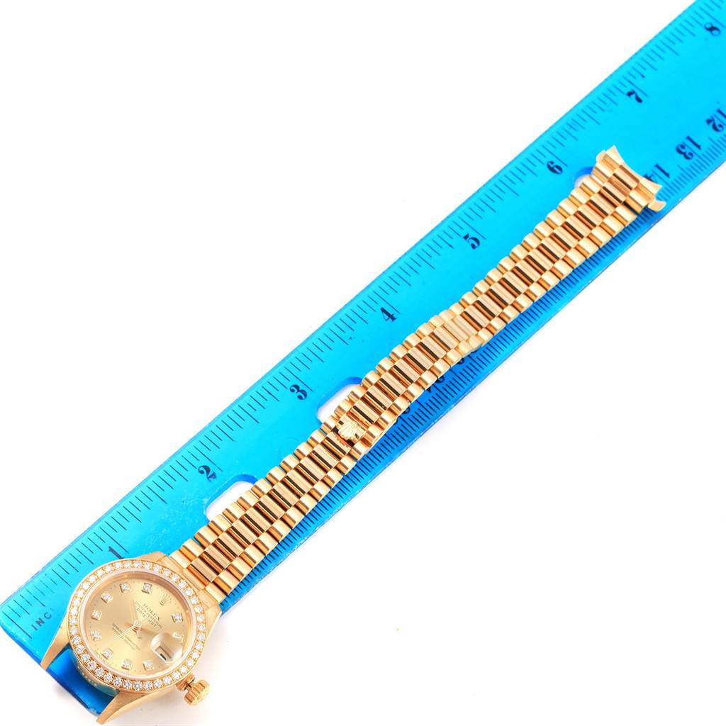 The Rolex President 79138 Women's Yellow Gold Champagne Dial 79138 Women's Yellow Gold Champagne Dial model watch is shown laid flat next to a blue ruler, displaying the face and full bracelet.