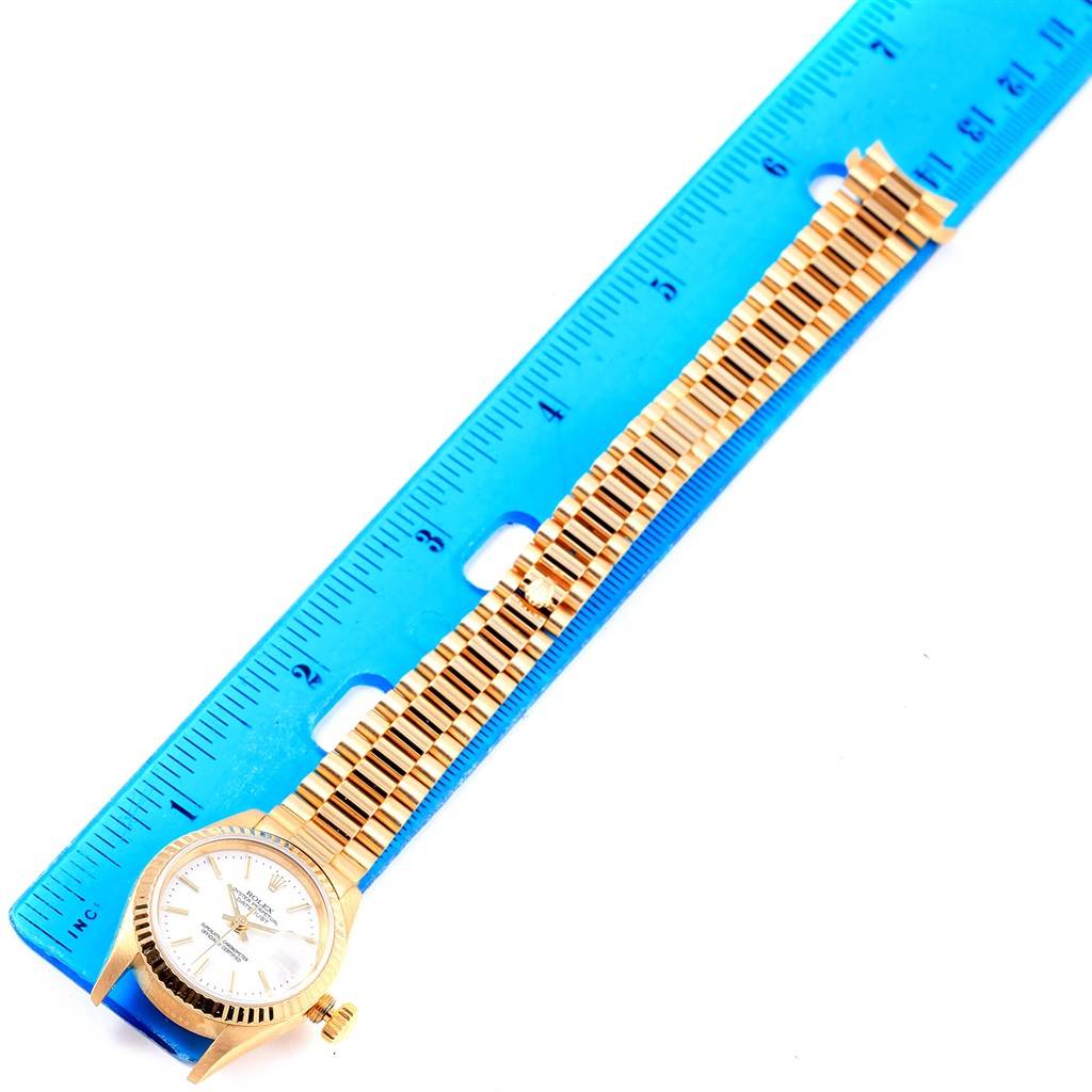 The image displays a Rolex President 79178 Women's Yellow Gold White Dial 79178 Women's Yellow Gold White Dial model watch laid flat next to a ruler, showing the entire band and dial.