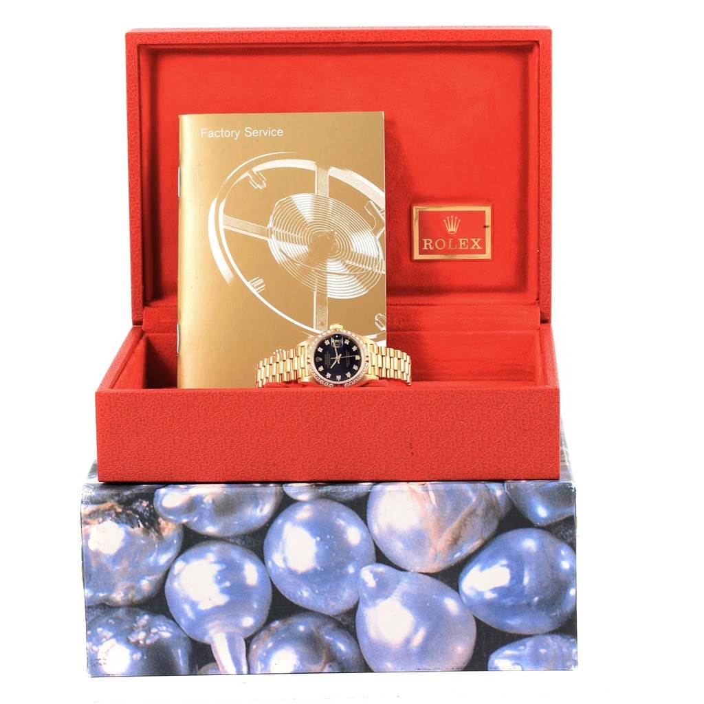 The image shows a Rolex President 69258 Women's Yellow Gold Black Dial 69258 Women's Yellow Gold Black Dial model watch inside a red box, accompanied by a Factory Service booklet.