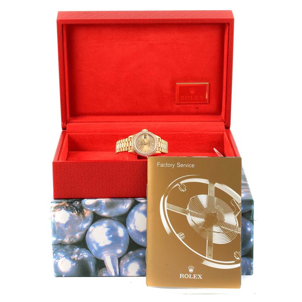 The image shows a Rolex President 69178 Women
s Yellow Gold Champagne Dial 69178 Women
s Yellow Gold Champagne Dial model watch in a red box, with a Factory Service booklet in front of it.