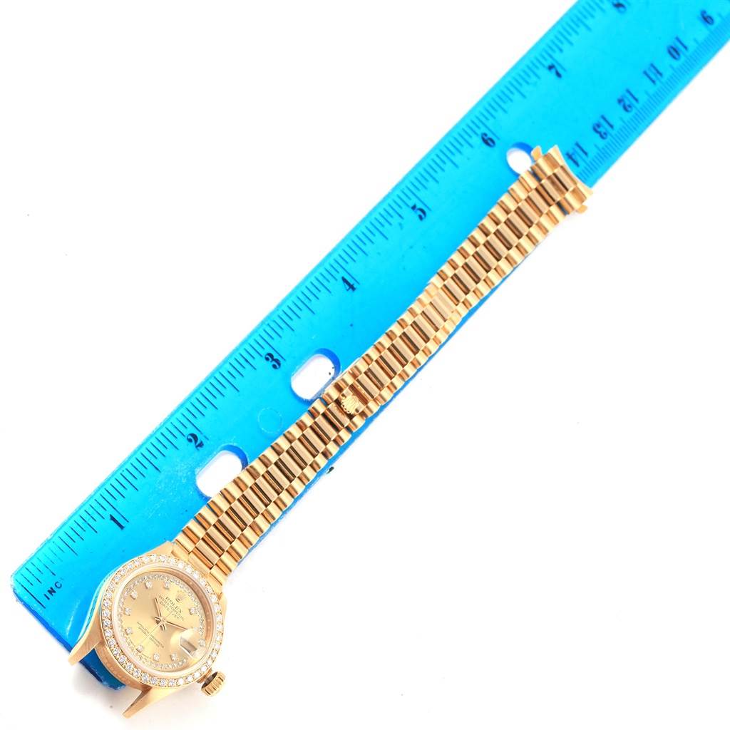 The image shows a Rolex President 69178 Women
s Yellow Gold Champagne Dial 69178 Women
s Yellow Gold Champagne Dial model watch, featuring both the face and full bracelet, placed next to a blue ruler.