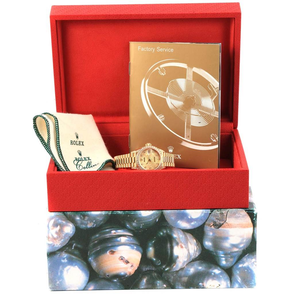 The image shows a Rolex President 69158 Women's Yellow Gold Champagne Dial 69158 Women's Yellow Gold Champagne Dial model watch inside an open red box, along with a manual and a branded cloth.