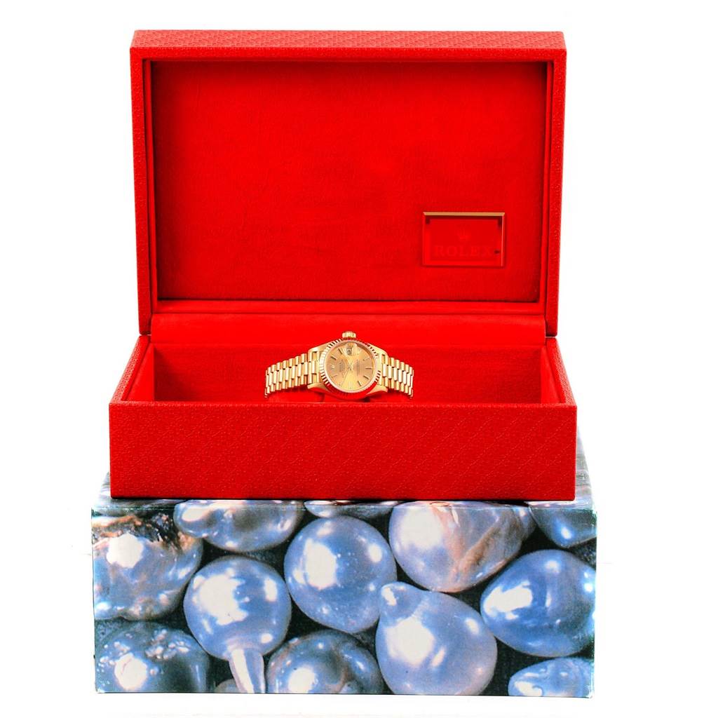 This Rolex President 69178 Women's Yellow Gold Champagne Dial 69178 Women's Yellow Gold Champagne Dial model watch is shown from the front, placed inside an open red watch box, resting on a decorated base.