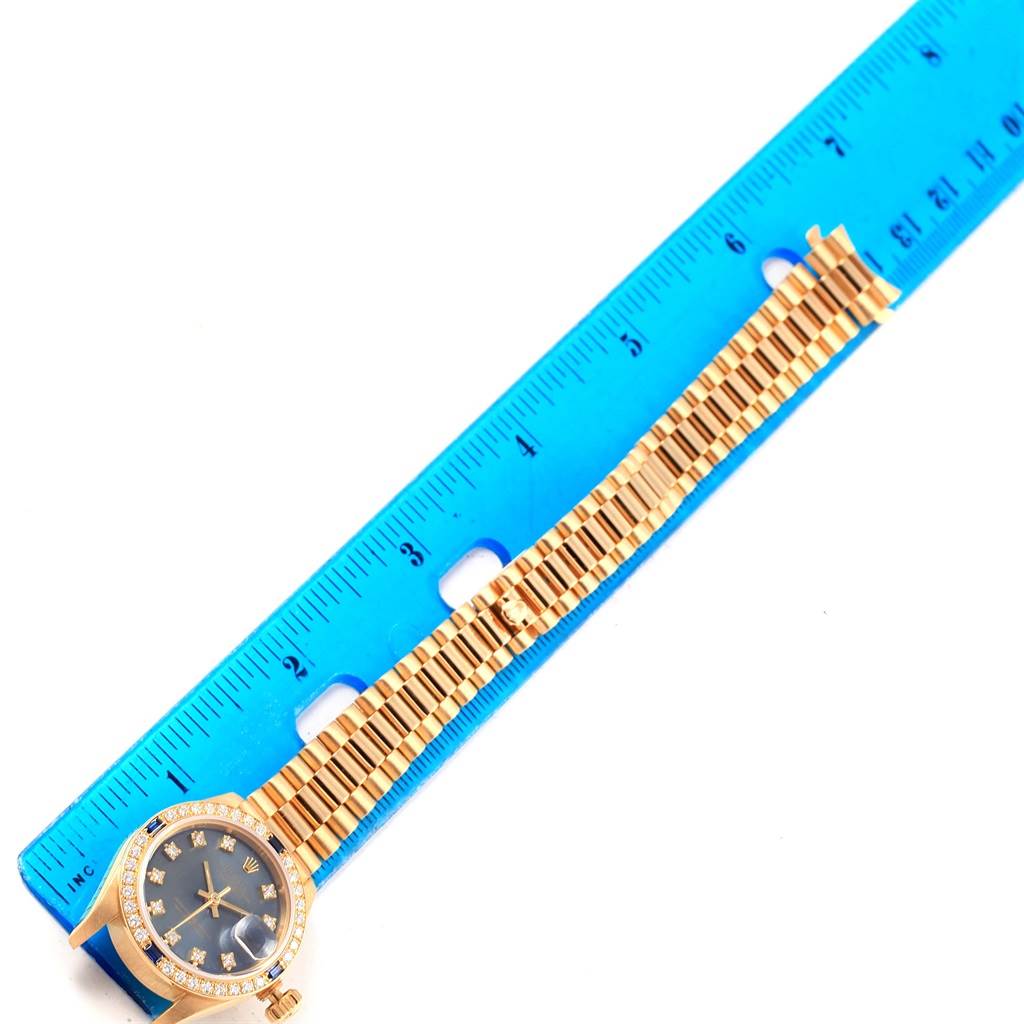 The image shows a top-down view of a Rolex President 69088 Women's Yellow Gold Blue Dial 69088 Women's Yellow Gold Blue Dial model watch, highlighting the watch face and metal bracelet next to a blue ruler.