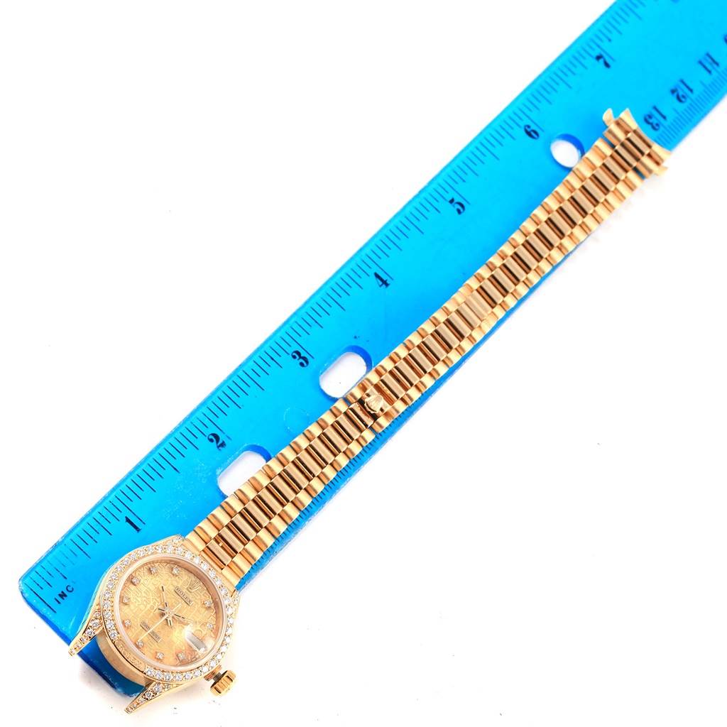 The image shows the face and bracelet of a Rolex President 69198 Women
s Yellow Gold Champagne Dial 69198 Women
s Yellow Gold Champagne Dial watch next to a blue ruler, taken from a top-down angle.