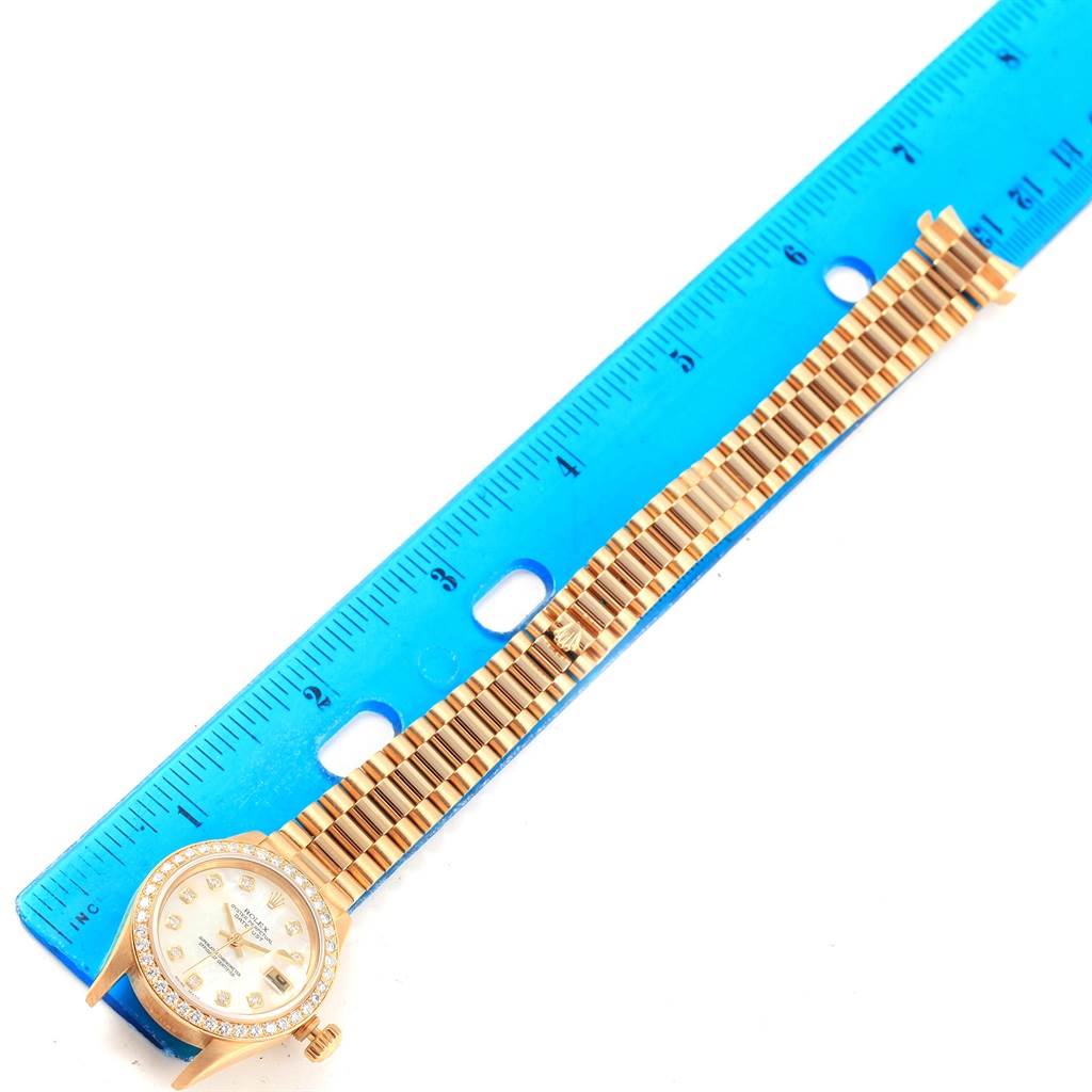 The image shows a Rolex President 79138 Women
s Yellow Gold Champagne Dial 79138 Women
s Yellow Gold Champagne Dial model watch laid flat beside a blue ruler, highlighting the face and bracelet.