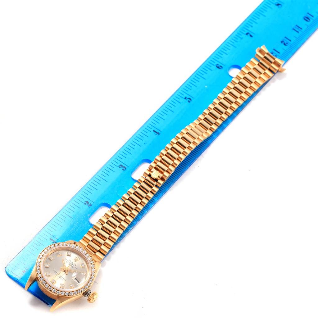 The image shows a Rolex President 69138 Women's Yellow Gold Silver Dial 69138 Women's Yellow Gold Silver Dial model watch laid flat with its gold bracelet extended alongside a blue ruler for measurement.