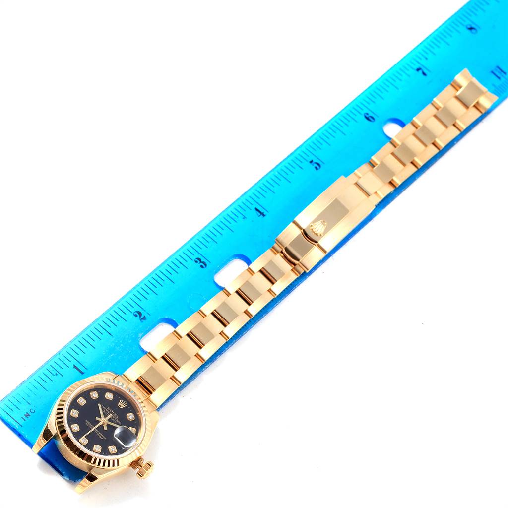The image shows a Rolex President 179178 Women's Yellow Gold Black Dial 179178 Women's Yellow Gold Black Dial model watch laid flat next to a blue ruler, displaying its band and face.