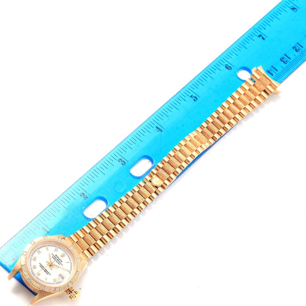 The Rolex President 69288 Women
s Yellow Gold White Dial 69288 Women
s Yellow Gold White Dial model watch is shown from the top, displaying the face, bezel, and full metal band next to a ruler.