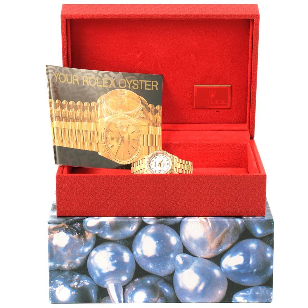 The image shows a Rolex President 69288 Women
s Yellow Gold White Dial 69288 Women
s Yellow Gold White Dial watch with its bracelet, placed inside an open red case alongside a brochure.