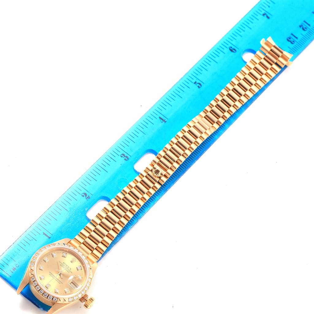The image shows a Rolex President 79268 Women
s Yellow Gold Champagne Dial 79268 Women
s Yellow Gold Champagne Dial model watch, displaying the full length of the band and watch face, positioned next to a blue ruler.