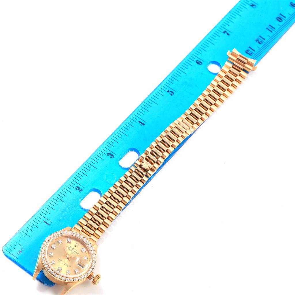 The image shows a Rolex President 69138 Women
s Yellow Gold Champagne Dial 69138 Women
s Yellow Gold Champagne Dial model watch laid flat beside a blue ruler, displaying its face and full bracelet.