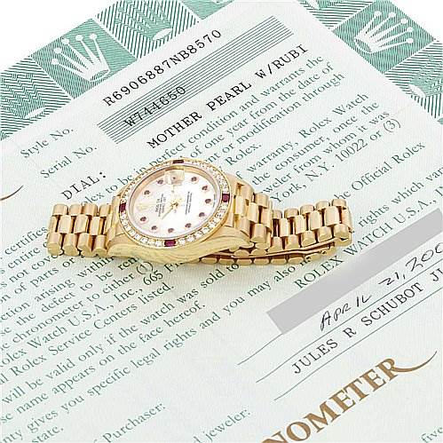 The image shows a Rolex President 69068 Women
s Yellow Gold Mother of Pearl Dial 69068 Women
s Yellow Gold Mother of Pearl Dial model watch lying flat on its side, displaying its gold bracelet and round face with ruby indices.