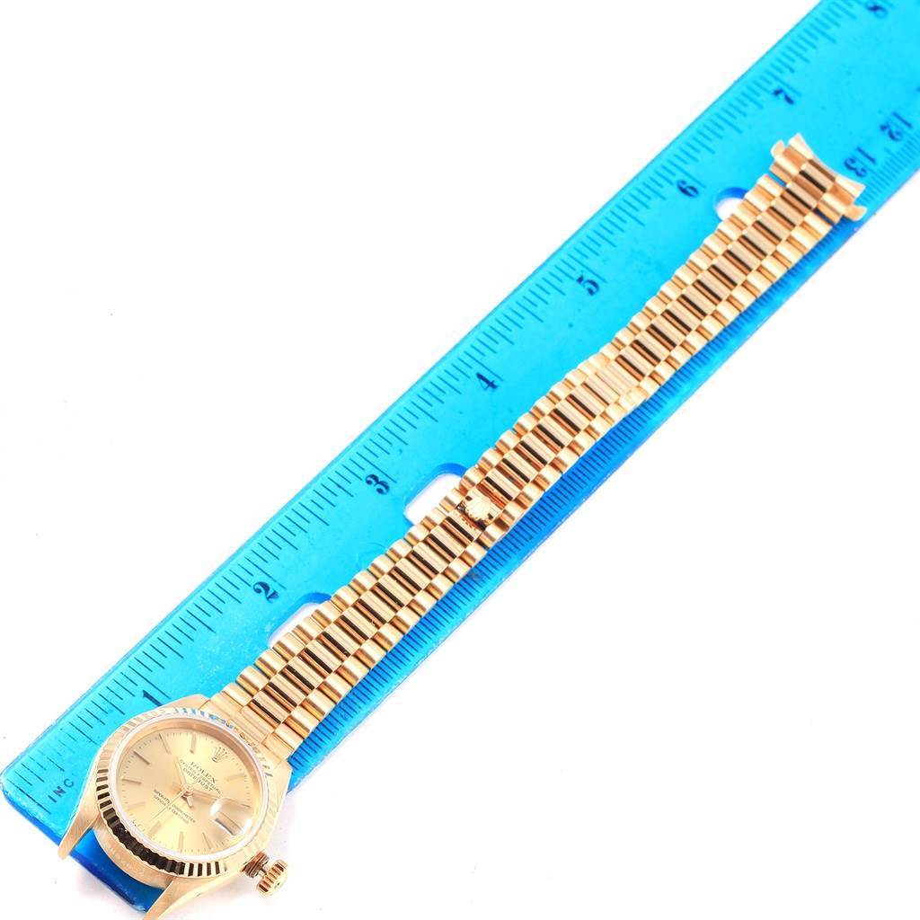 The image shows a Rolex President 69178 Women
s Yellow Gold Champagne Dial 69178 Women
s Yellow Gold Champagne Dial model watch laid flat with its bracelet next to a blue ruler for scale.