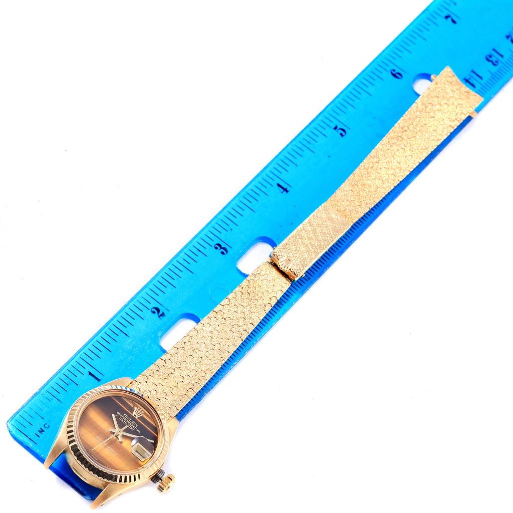 The watch shown is a Rolex President 6917 Women's Yellow Gold Brown Dial 6917 Women's Yellow Gold Brown Dial model, displayed flat with a gold band and face next to a blue ruler for scale.