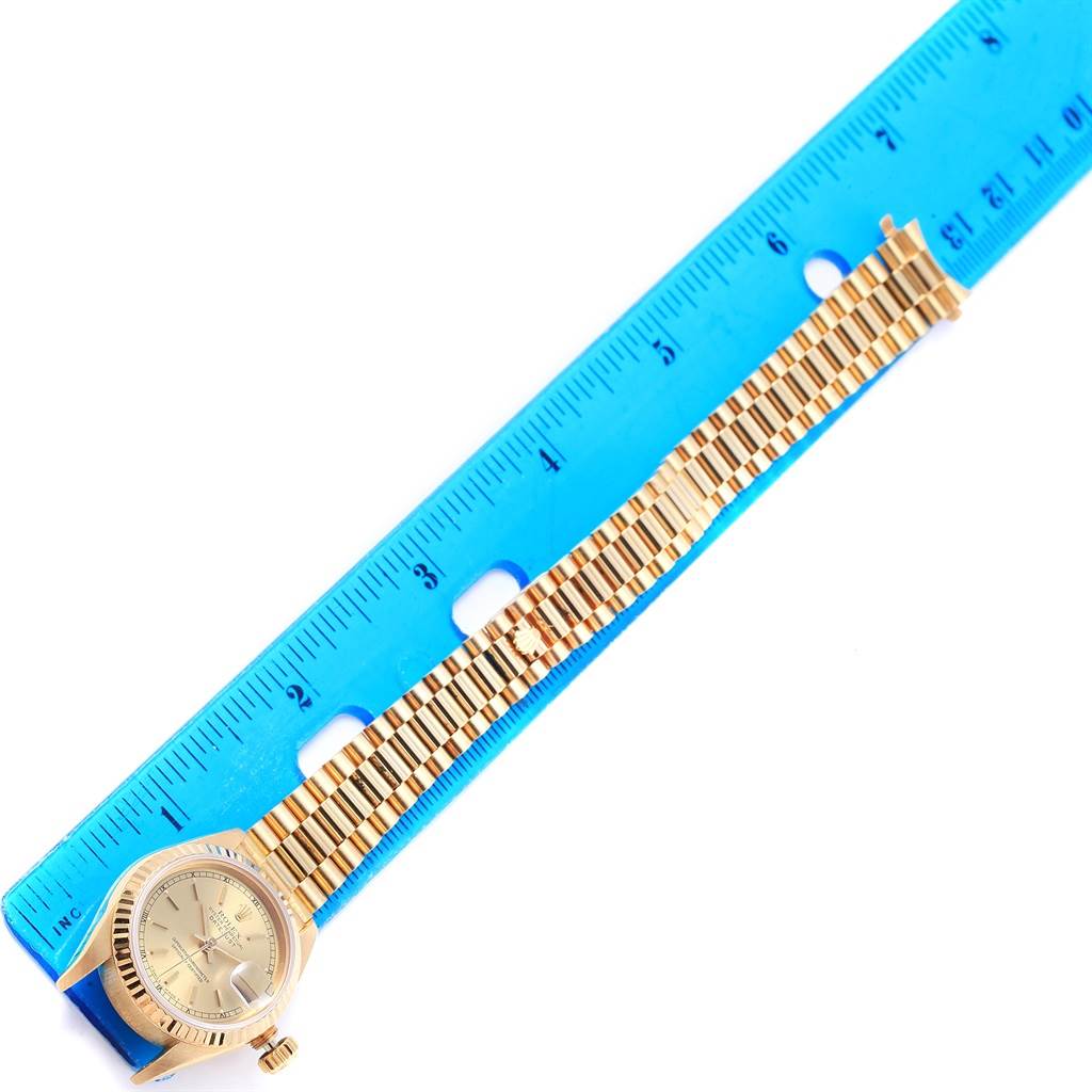 The image shows a Rolex President 69178 Women
s Yellow Gold Champagne Dial 69178 Women
s Yellow Gold Champagne Dial model watch laid flat next to a blue ruler, displaying its face and band.