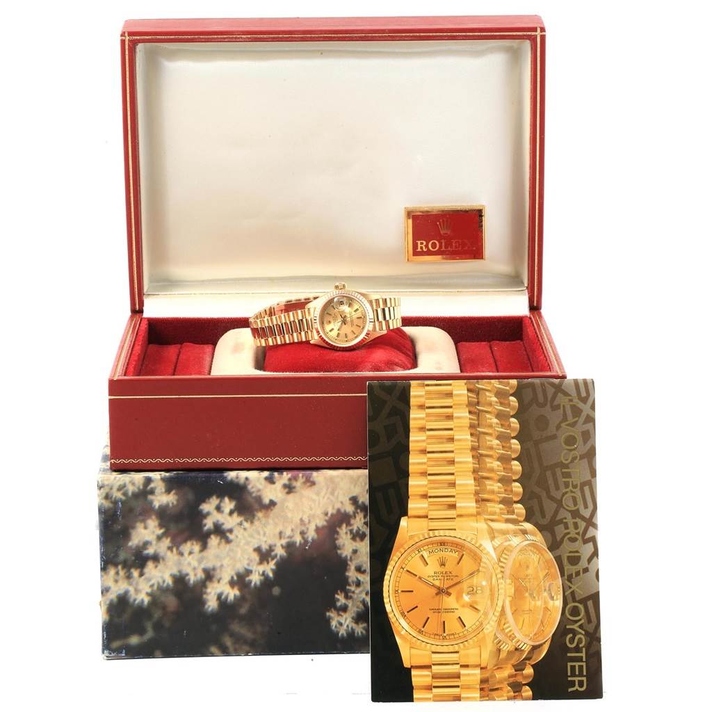The image shows a Rolex President 69178 Women
s Yellow Gold Champagne Dial 69178 Women
s Yellow Gold Champagne Dial model watch in an open box with a catalog or booklet in front.