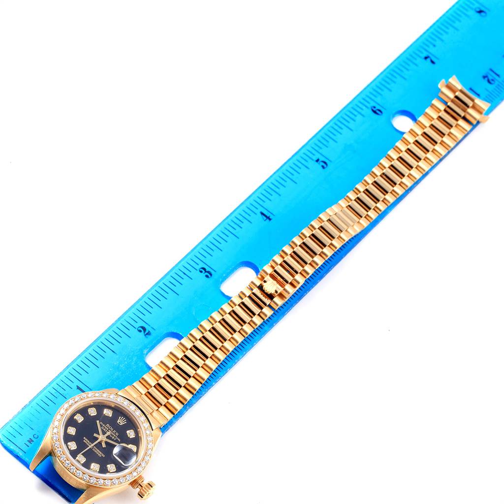 The image shows a Rolex President 69138 Women
s Yellow Gold Black Dial 69138 Women
s Yellow Gold Black Dial watch laid flat against a blue ruler, displaying the watch face and entire bracelet.
