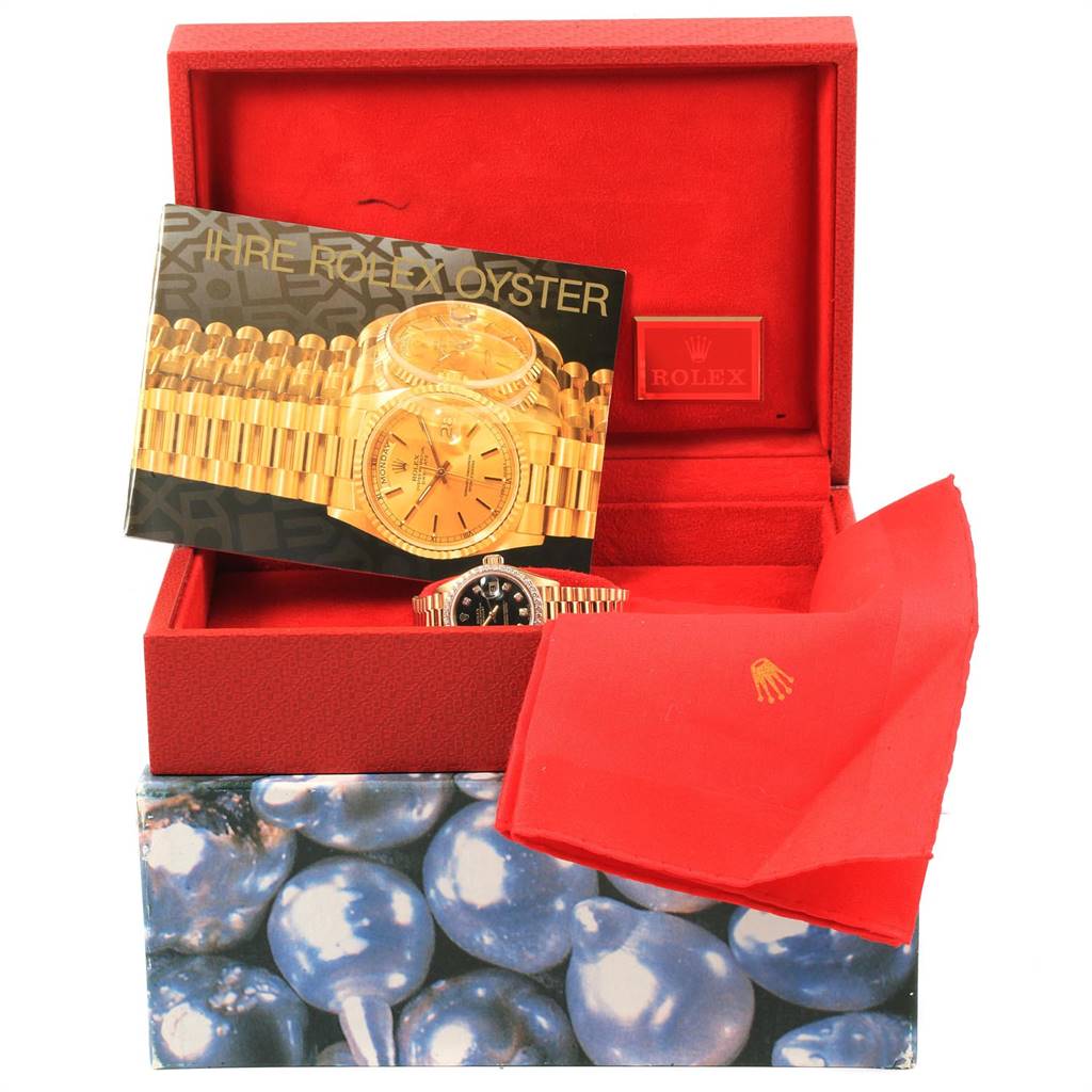 The image shows a Rolex President 69138 Women
s Yellow Gold Black Dial 69138 Women
s Yellow Gold Black Dial model watch partially visible in its open, red box with a booklet and a cleaning cloth.