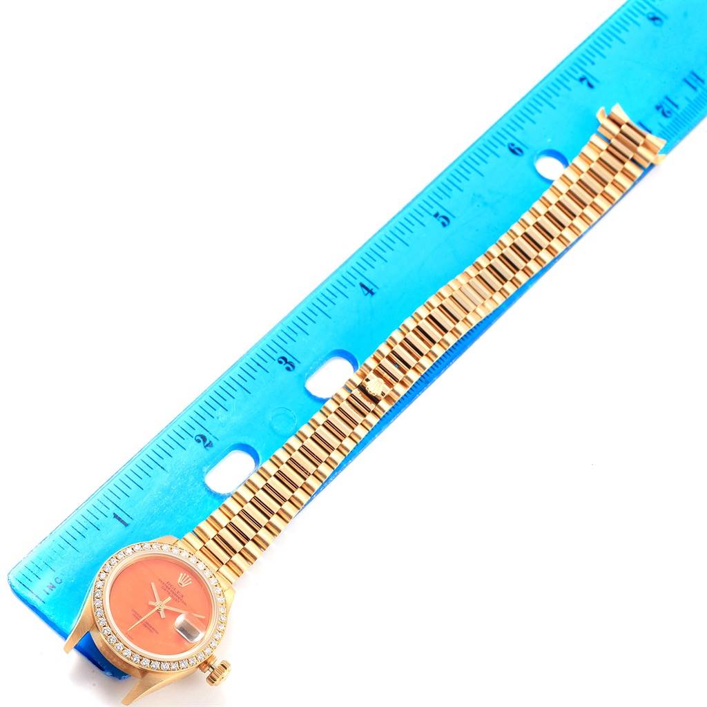 The image shows a Rolex President 69178 Women's Yellow Gold Orange Dial 69178 Women's Yellow Gold Orange Dial model watch with its band measured against a blue ruler.