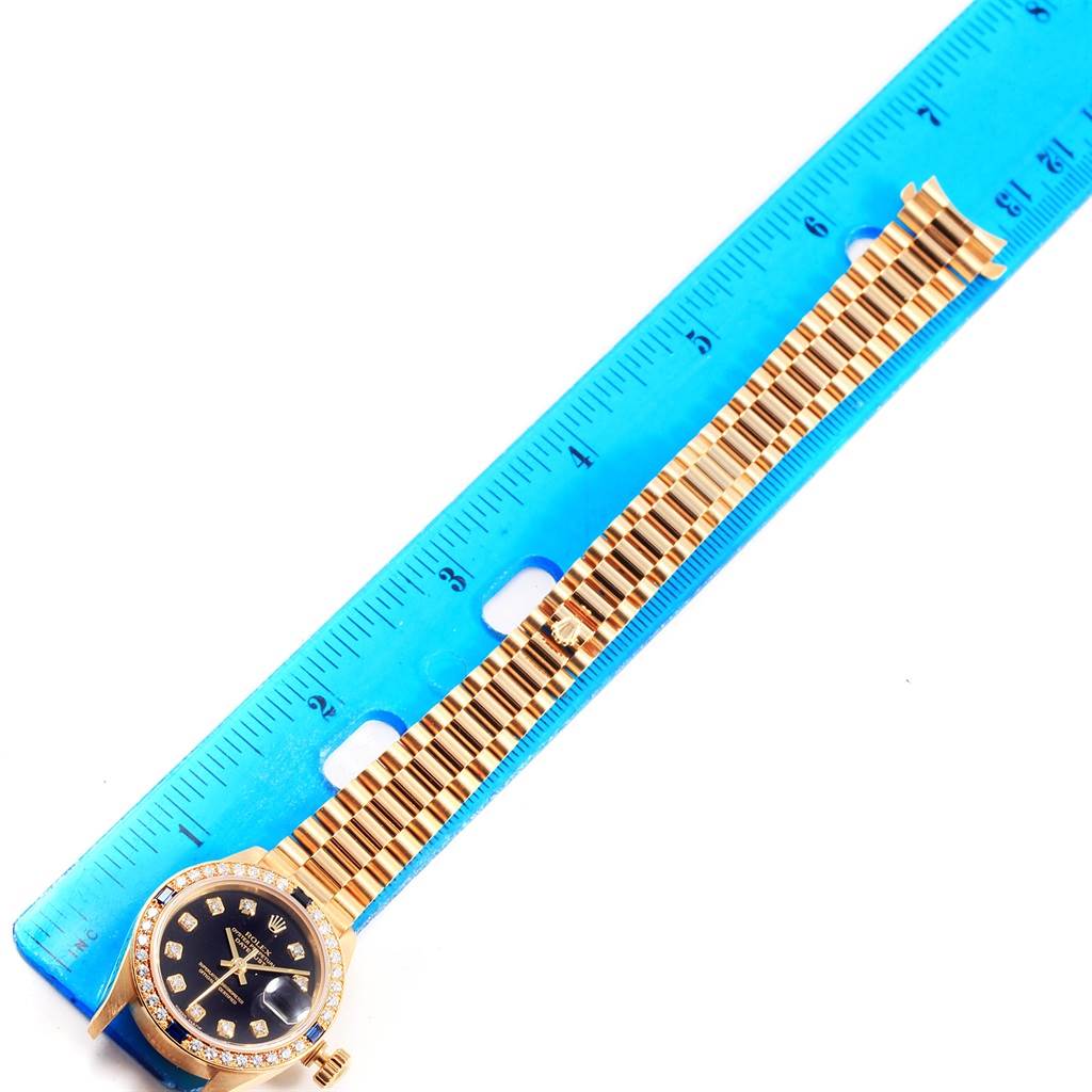 The image shows a Rolex President 79088 Women's Yellow Gold Black Dial 79088 Women's Yellow Gold Black Dial model watch laid flat beside a blue ruler, displaying the watch face and bracelet.