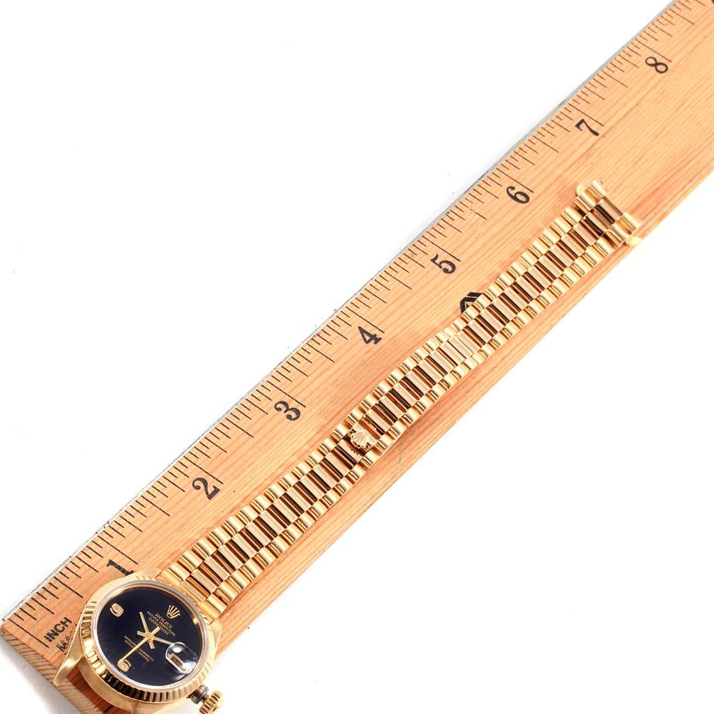 The image shows a Rolex President 69178 Women's Yellow Gold Black Dial 69178 Women's Yellow Gold Black Dial model, taken at a top-down angle with the watch face, band, and a wooden ruler.