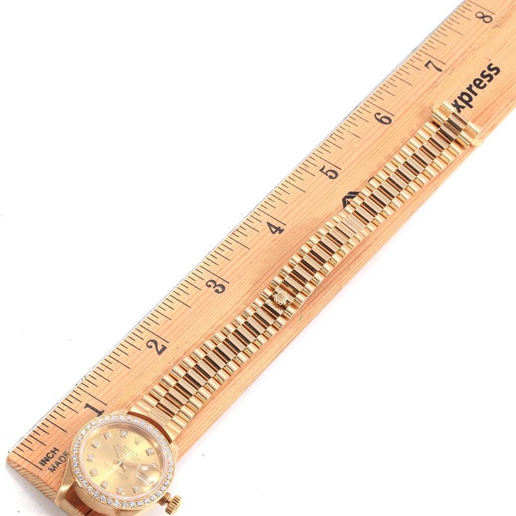 The image shows a Rolex President 79178 Women
s Yellow Gold Champagne Dial 79178 Women
s Yellow Gold Champagne Dial model watch laid flat next to a ruler, displaying its dial, bezel, and bracelet.