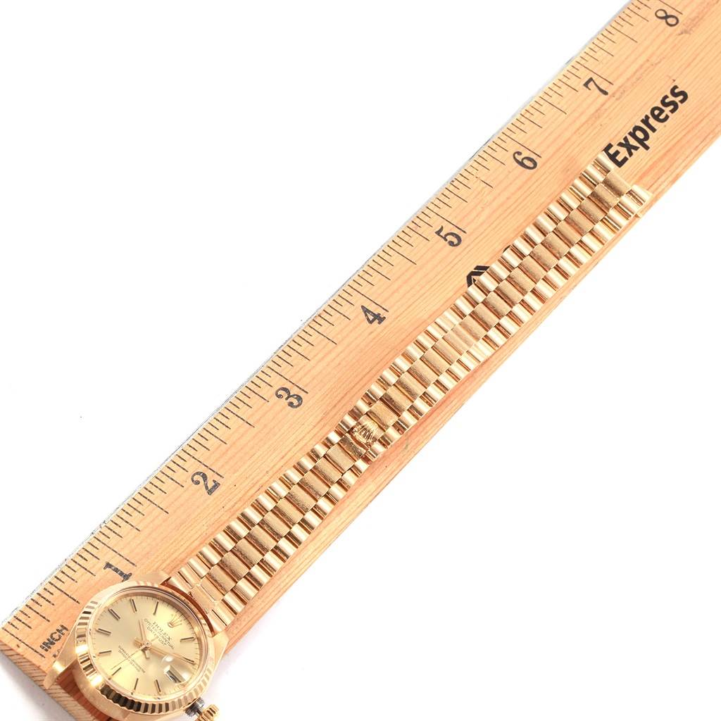The image shows the face and band of a Rolex President 6917 Women's Yellow Gold Champagne Dial 6917 Women's Yellow Gold Champagne Dial model watch positioned next to a wooden ruler.