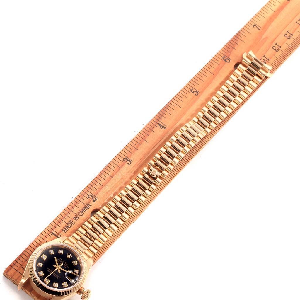 The image shows a Rolex President 69178 Women's Yellow Gold Black Dial 69178 Women's Yellow Gold Black Dial model watch laid flat next to a ruler, displaying its face and metal bracelet.