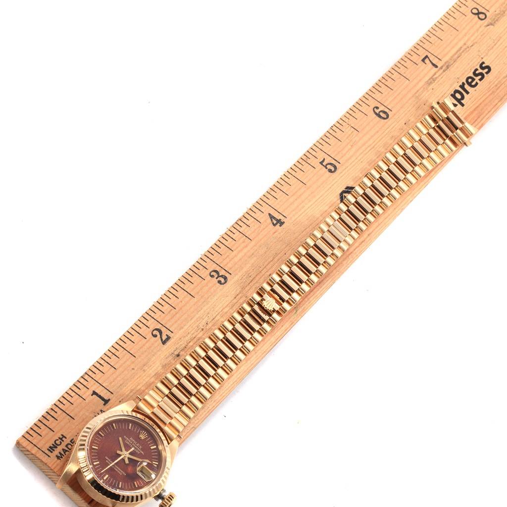 The Rolex President 6917 Women's Yellow Gold Brown Dial 6917 Women's Yellow Gold Brown Dial watch is shown from above with its dial, case, and bracelet placed alongside a ruler for measurement.