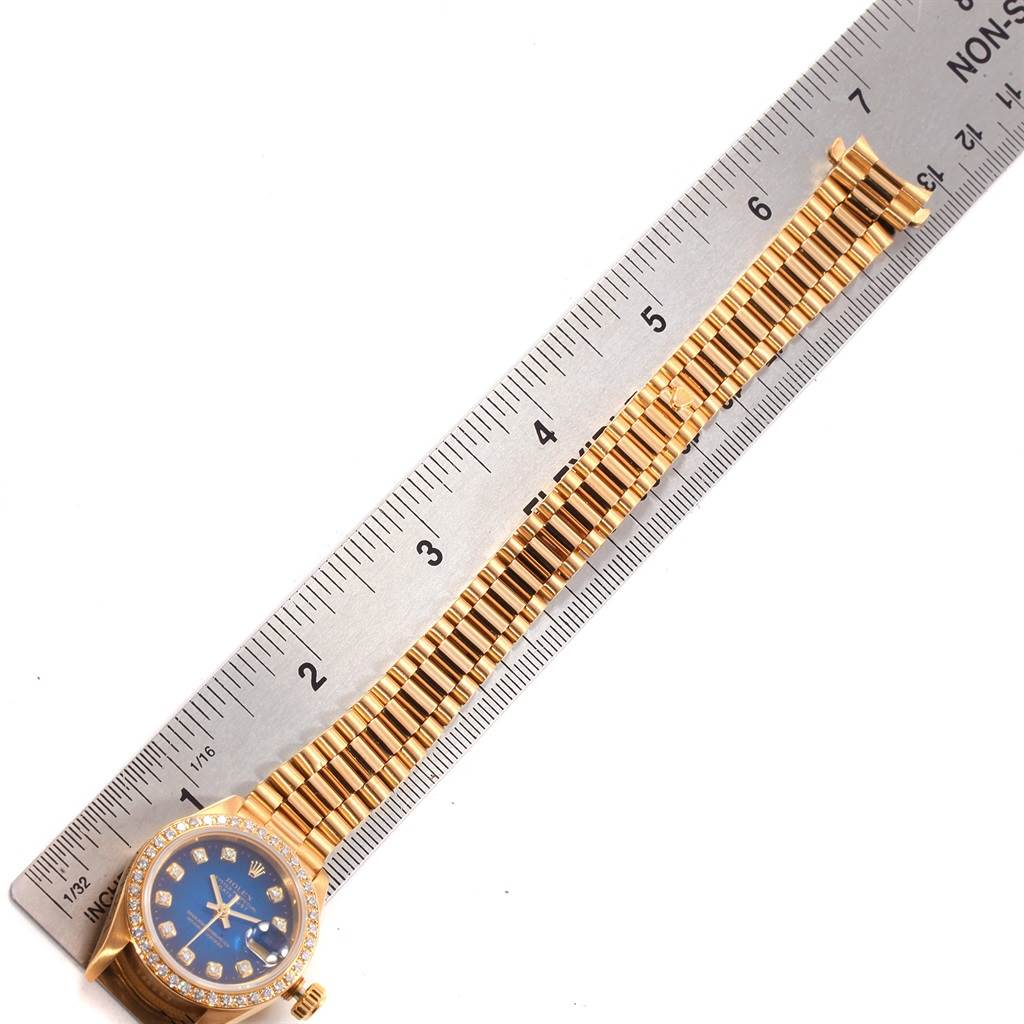 The image shows a Rolex President 69138 Women's Yellow Gold Blue Dial 69138 Women's Yellow Gold Blue Dial model watch laid flat with a blue dial against a ruler, showcasing its bracelet and bezel.