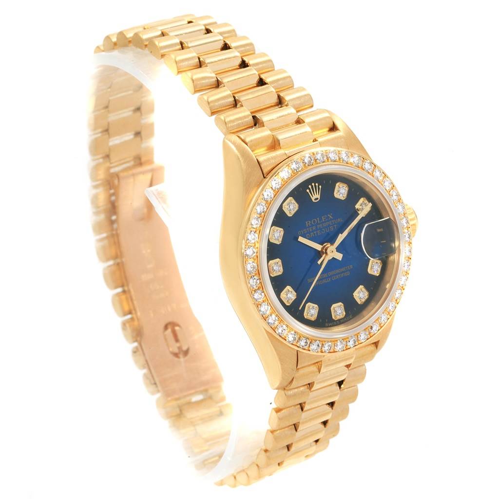 The image shows a Rolex President 69138 Women's Yellow Gold Blue Dial 69138 Women's Yellow Gold Blue Dial model watch angled to reveal its face, gold bracelet, and bejeweled bezel.