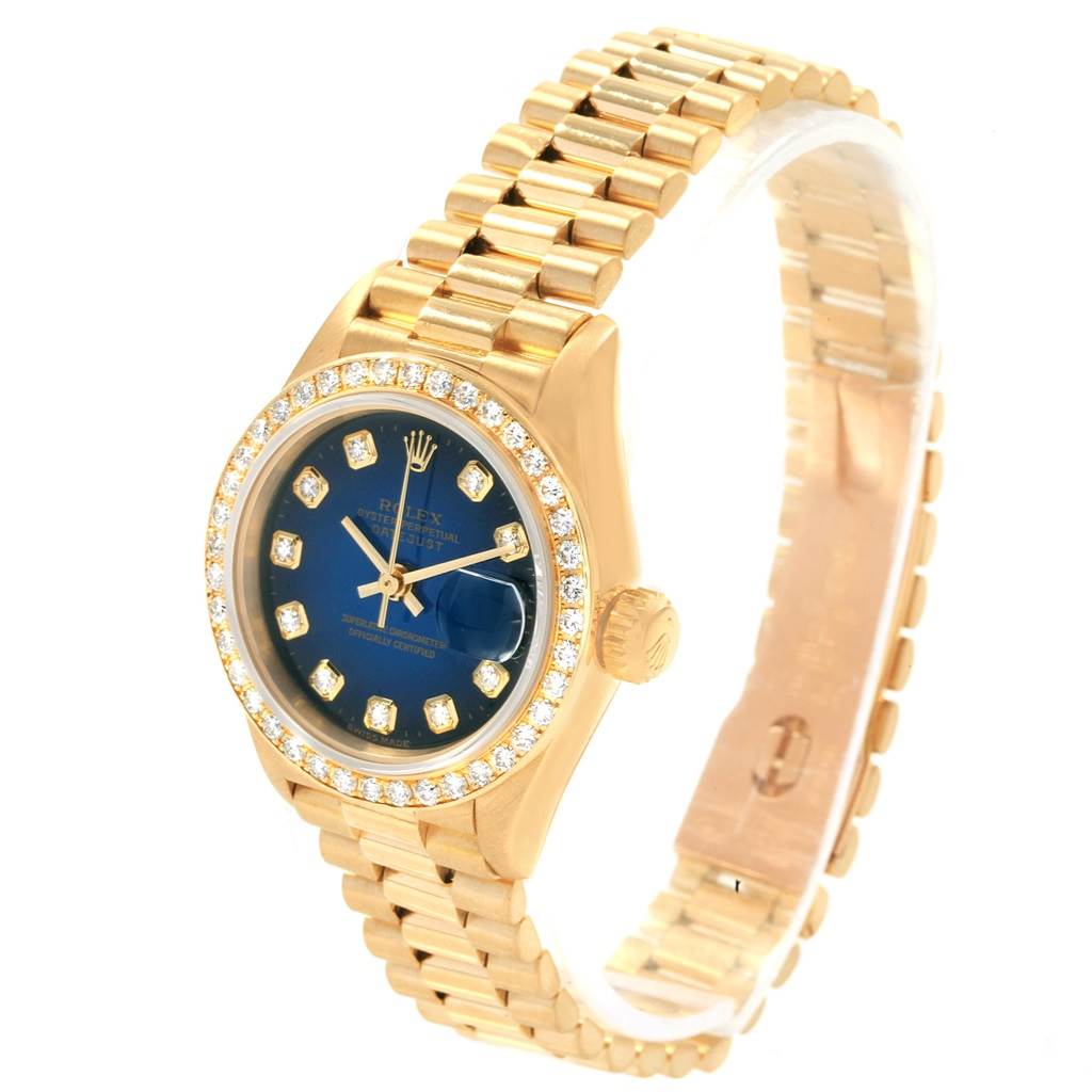 The Rolex President 69138 Women's Yellow Gold Blue Dial 69138 Women's Yellow Gold Blue Dial model watch is shown at an angled view, displaying its gold case, diamond bezel, blue dial, and gold bracelet.