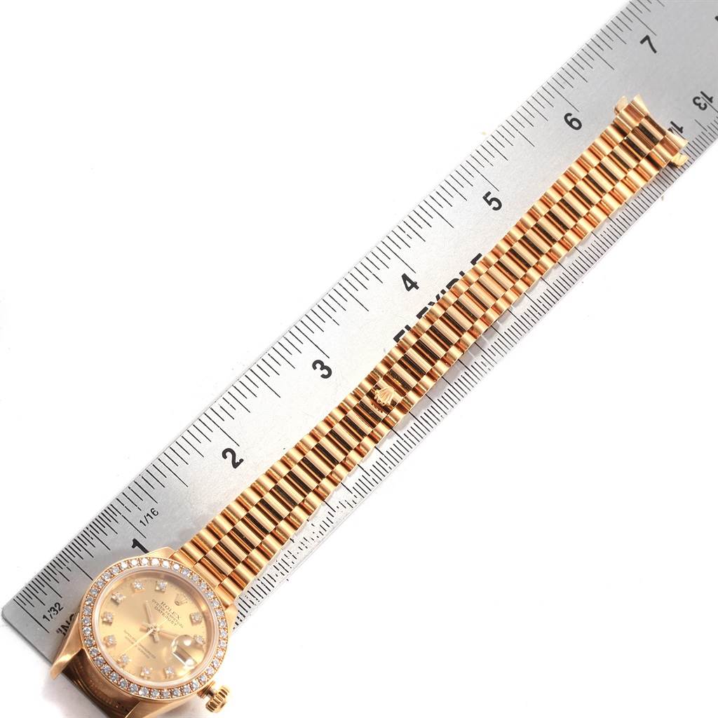 This image shows the Rolex President 69178 Women's Yellow Gold Champagne Dial 69178 Women's Yellow Gold Champagne Dial model watch from an overhead angle, displaying its face, bezel, and metal bracelet alongside a measuring ruler.