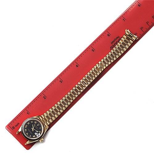The Rolex President 69068 Women's Yellow Gold Black Dial 69068 Women's Yellow Gold Black Dial model watch is shown laid flat next to a red ruler, displaying its entire band and face from above.