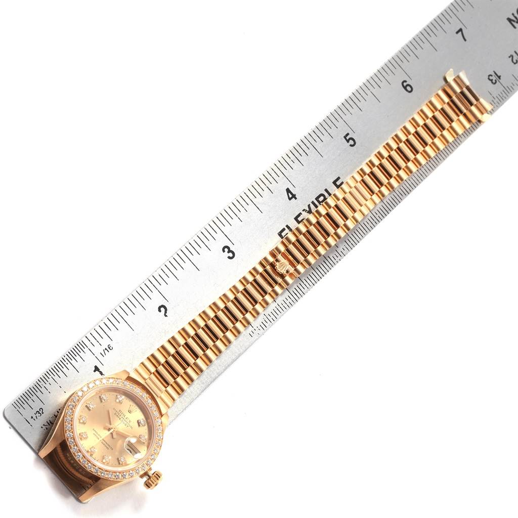The image shows a Rolex President 69178 Women's Yellow Gold Champagne Dial 69178 Women's Yellow Gold Champagne Dial model watch lying flat next to a ruler, showcasing its band and watch face.