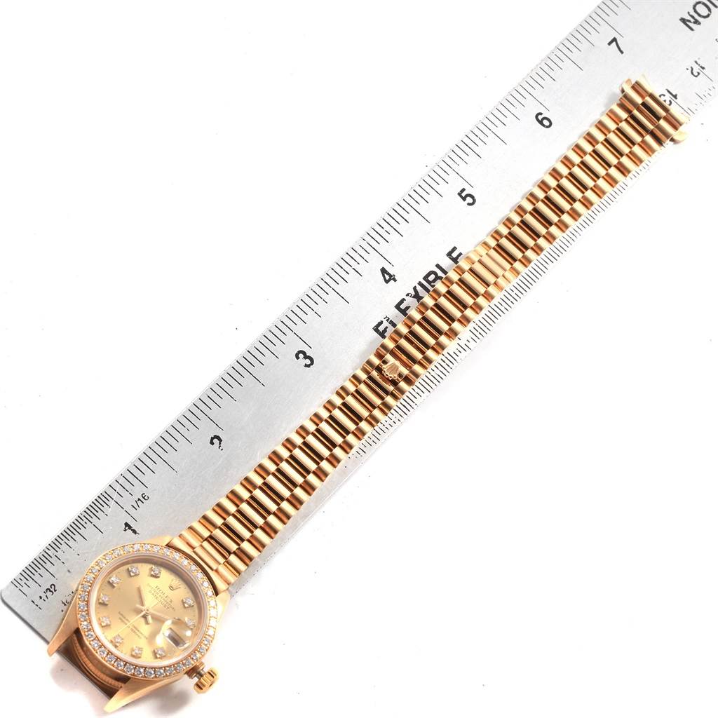 The image shows a Rolex President 69138 Women
s Yellow Gold Champagne Dial 69138 Women
s Yellow Gold Champagne Dial model watch laid flat next to a ruler, displaying the watch face and band.