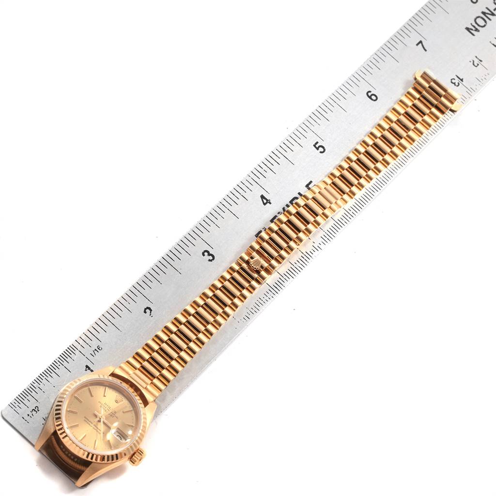 This image shows a Rolex President 69178 Women
s Yellow Gold Champagne Dial 69178 Women
s Yellow Gold Champagne Dial watch laid flat alongside a ruler for measurement.