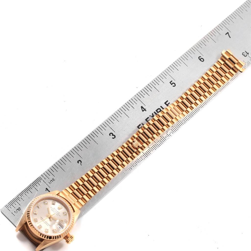 The image shows a Rolex President 69178 Women
s Yellow Gold Silver Dial 69178 Women
s Yellow Gold Silver Dial model watch laid flat next to a ruler, displaying its bracelet and face from a top-down angle.