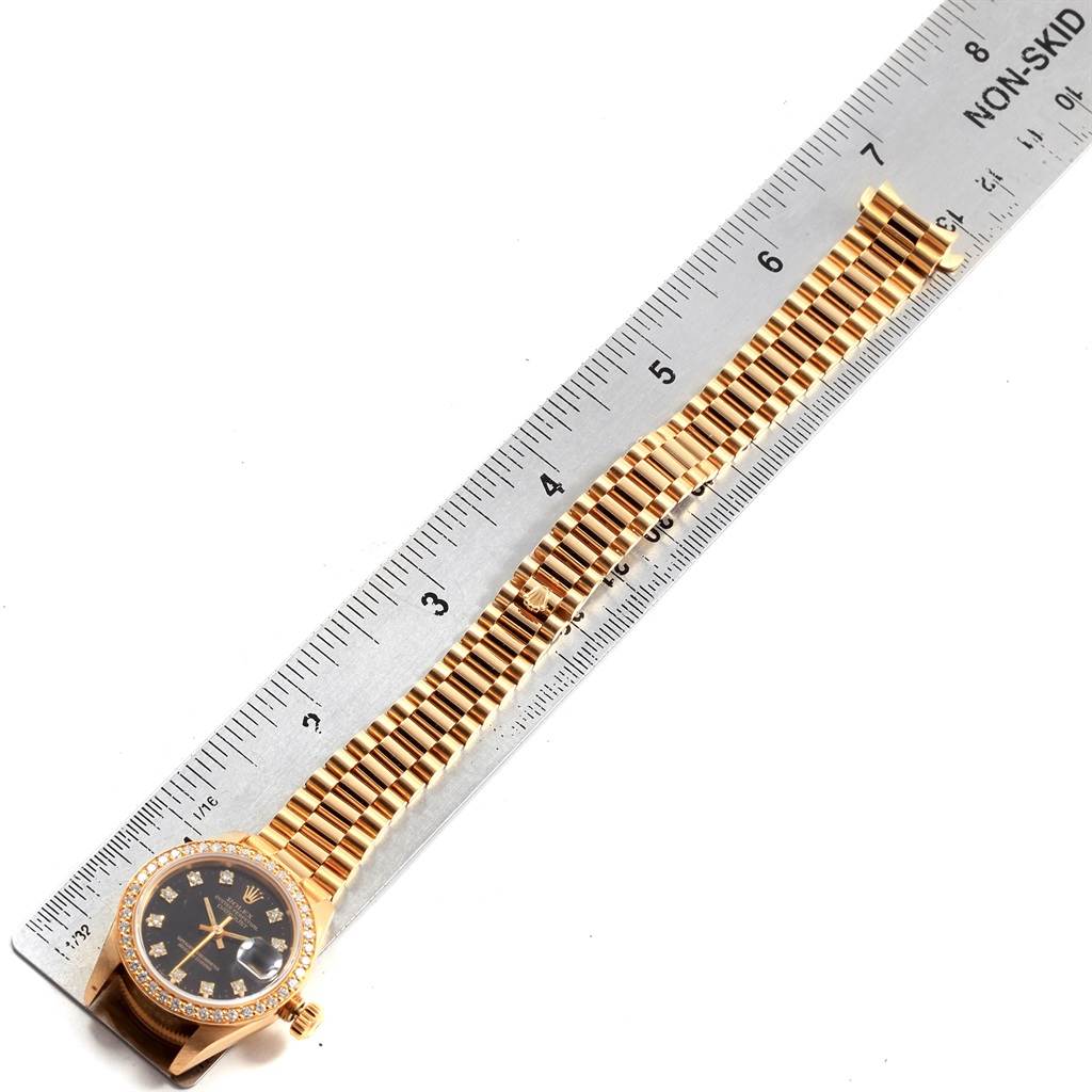 The image shows a Rolex President 69138 Women's Yellow Gold Black Dial 69138 Women's Yellow Gold Black Dial model watch lying flat next to a ruler, highlighting its face, bezel, and bracelet.