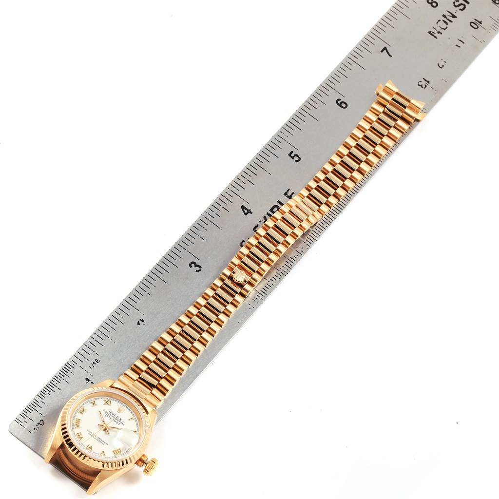 The image shows a Rolex President 69178 Women's Yellow Gold White Dial 69178 Women's Yellow Gold White Dial model watch horizontally next to a ruler, displaying its face and gold bracelet.