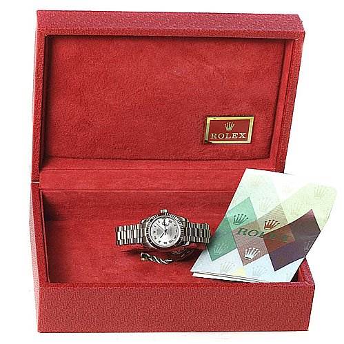 The image shows a President model Rolex watch in an open red box with a booklet beside it.