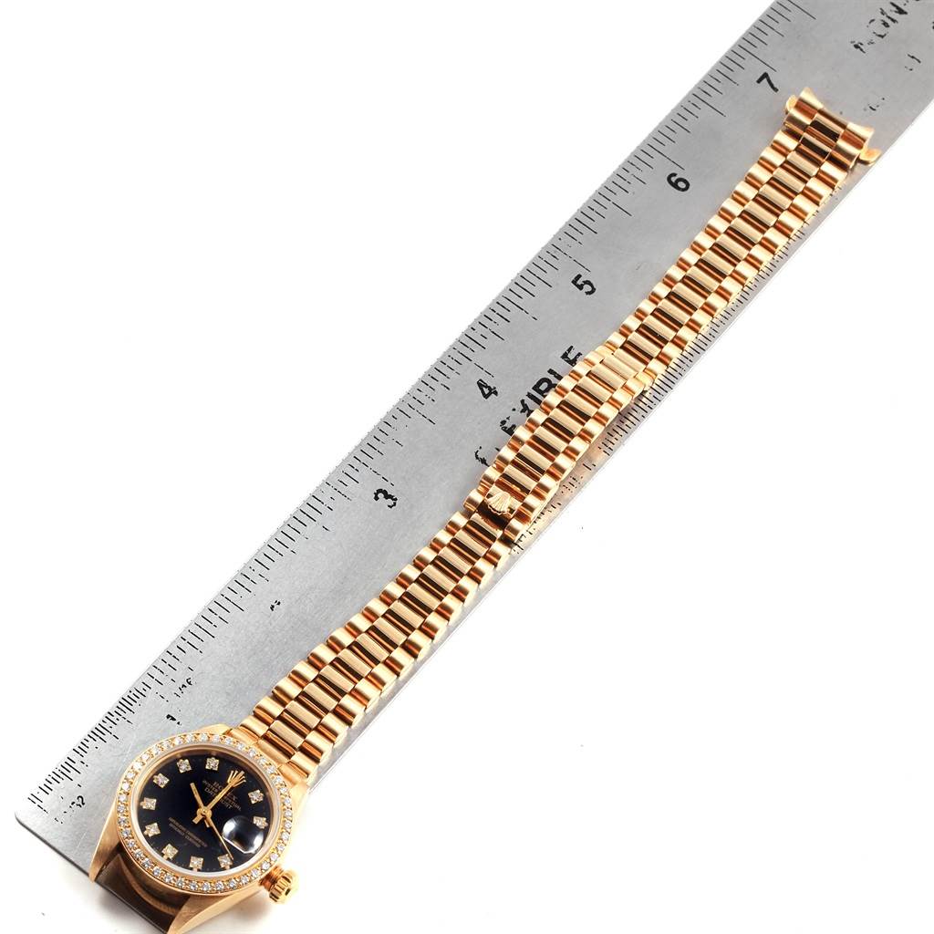 The image shows a Rolex President 69138 Women
s Yellow Gold Black Dial 69138 Women
s Yellow Gold Black Dial model watch laid flat alongside a ruler, showcasing the watch face and entire bracelet.