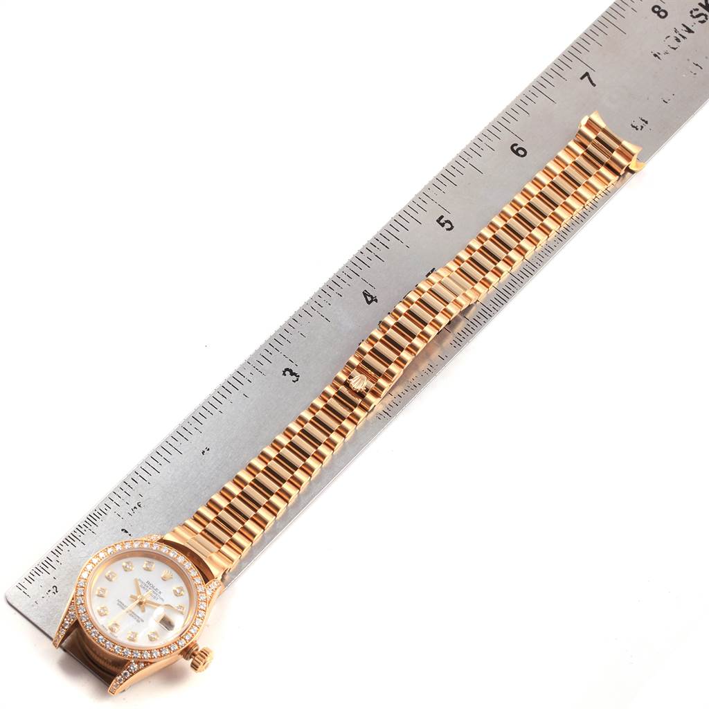 The image shows a Rolex President 69158 Women
s Yellow Gold Mother of Pearl Dial 69158 Women
s Yellow Gold Mother of Pearl Dial model watch laid flat, with the dial and full band visible next to a ruler for scale.