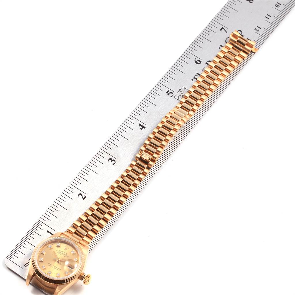 The image shows a Rolex President 69178 Women
s Yellow Gold Champagne Dial 69178 Women
s Yellow Gold Champagne Dial watch with a gold bracelet, lying flat next to a ruler for size reference.