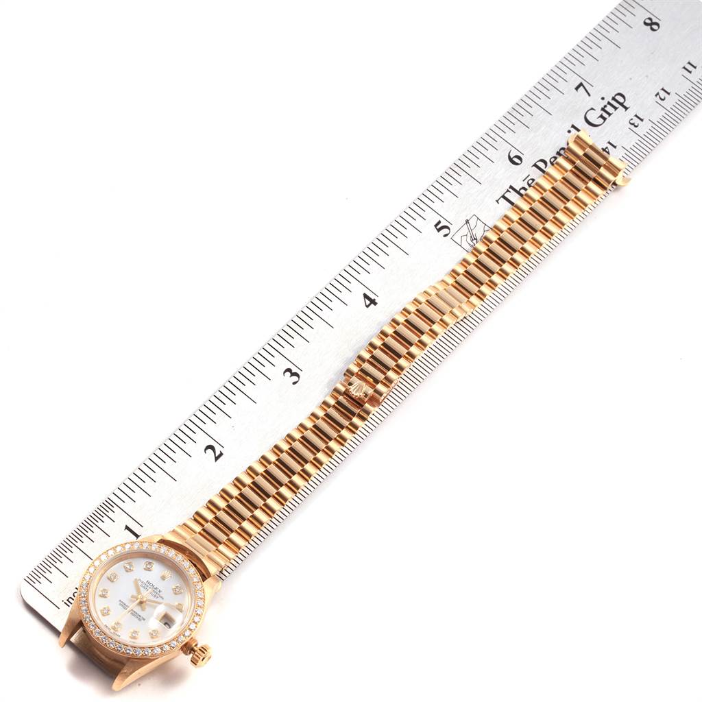 The image shows a Rolex President 69138 Women
s Yellow Gold Mother of Pearl Dial 69138 Women
s Yellow Gold Mother of Pearl Dial watch placed flat next to a ruler, displaying the face and bracelet.