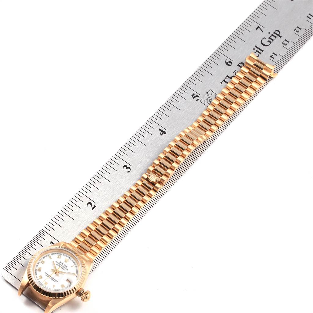 The image shows a Rolex President 69178 Women
s Yellow Gold White Dial 69178 Women
s Yellow Gold White Dial model watch lying flat next to a ruler, displaying its face and gold bracelet.