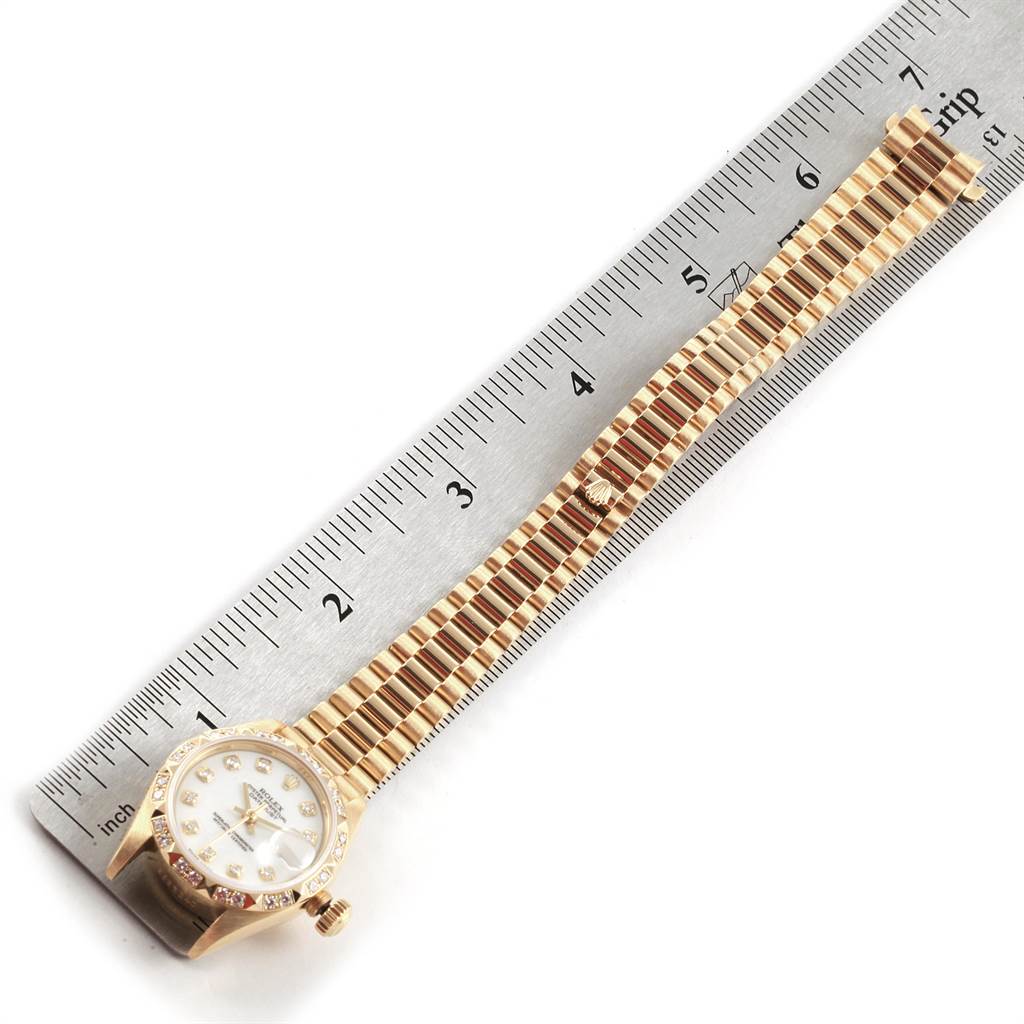 The image shows the Rolex President 69258 Women
s Yellow Gold White Dial 69258 Women
s Yellow Gold White Dial model watch laid flat next to a ruler for scale, displaying the face and full band.