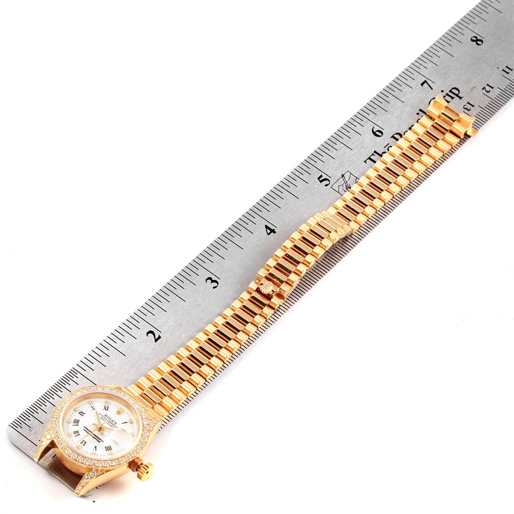 The image shows a Rolex President 69158 Women
s Yellow Gold White Dial 69158 Women
s Yellow Gold White Dial watch laid flat next to a ruler, displaying its face and bracelet in full.
