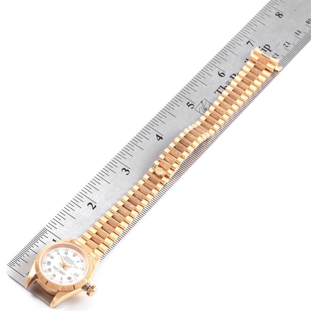 The image shows an overhead view of a Rolex President 69278 Women
s Yellow Gold White Dial 69278 Women
s Yellow Gold White Dial model watch, highlighting its gold bracelet laid next to a ruler.